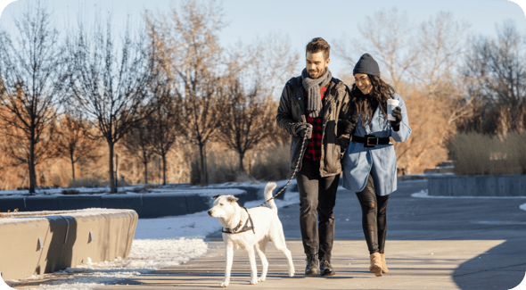 A couple walks a white dog in the park during early winter